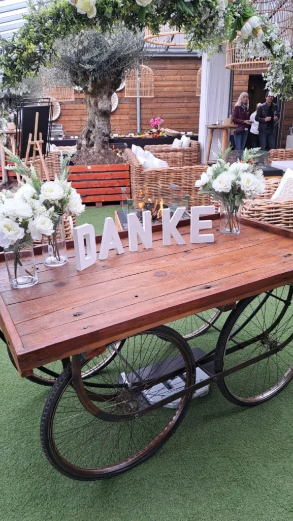 Holztisch auf Rädern mit Blumen und 'Danke'-Buchstaben