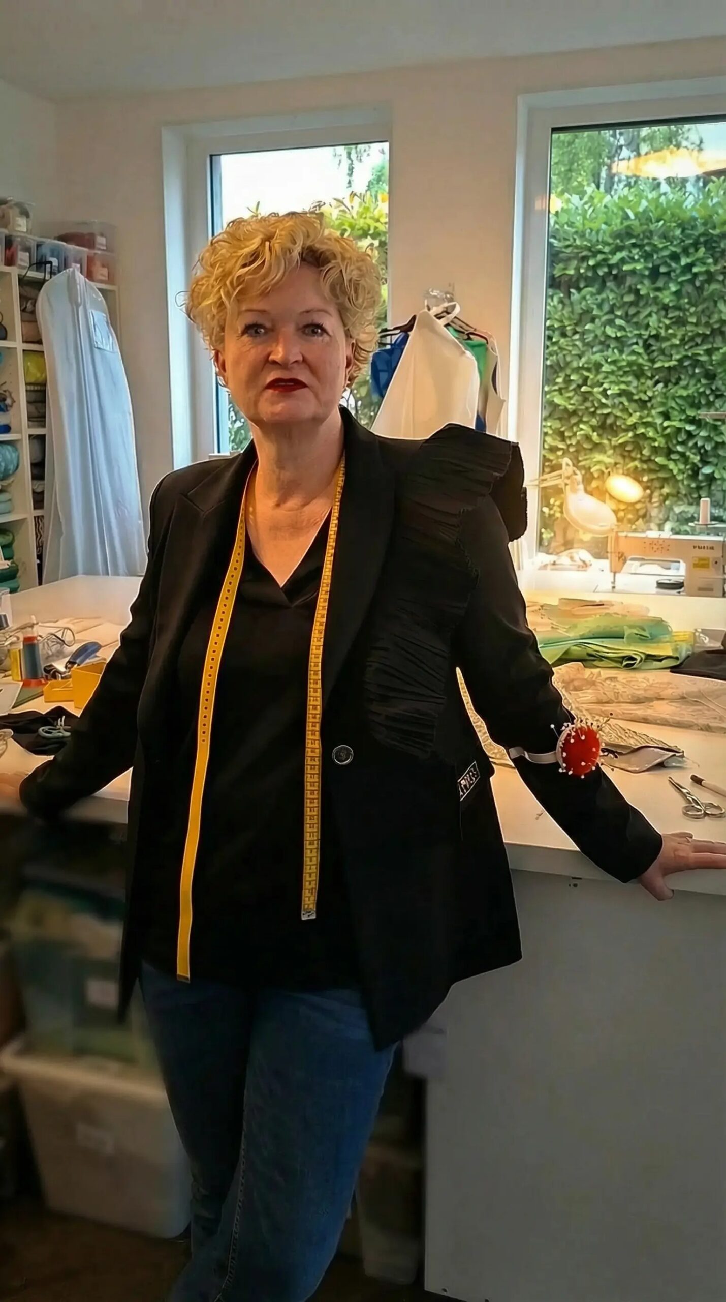Frau in Schneideratelier mit Maßband und Nadelkissen