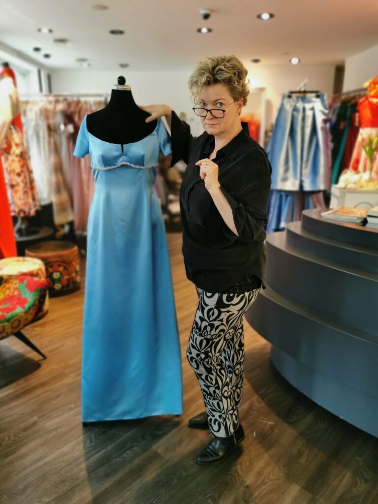 Silke-Scholz-Couture Frau neben Schneiderpuppe mit blauem Kleid in Modegeschäft