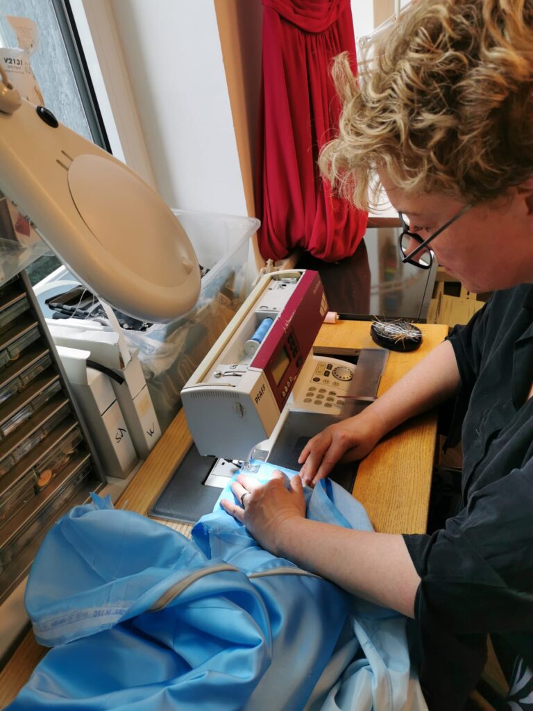 Silke-Scholz-Couture Person näht blauen Stoff an Nähmaschine